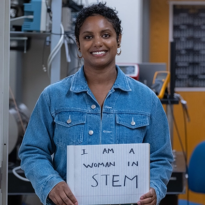 Alumna Brittany Karki holding a sign that says "I am a woman in STEM'