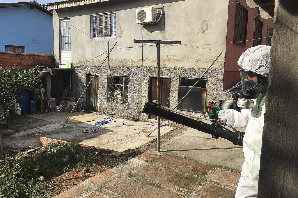 Worker in protective wear spraying to reduce mosquitos in an abandoned building complex.